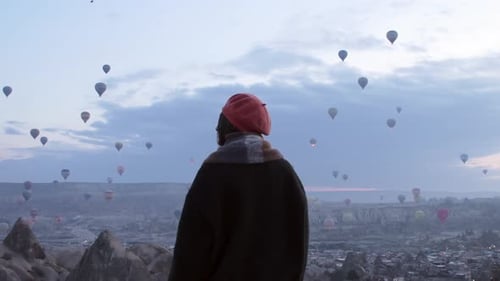 Woman Gazing at Hot Air Balloons Over Landscape