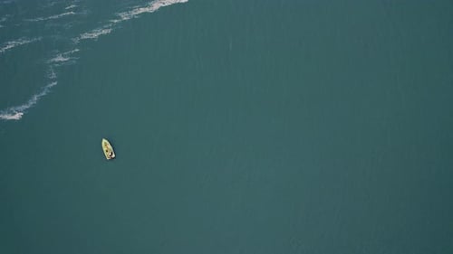 Aerial View of a Man in a Motorboat in the Turquoise Waters of the Bay and Waves with White Foam