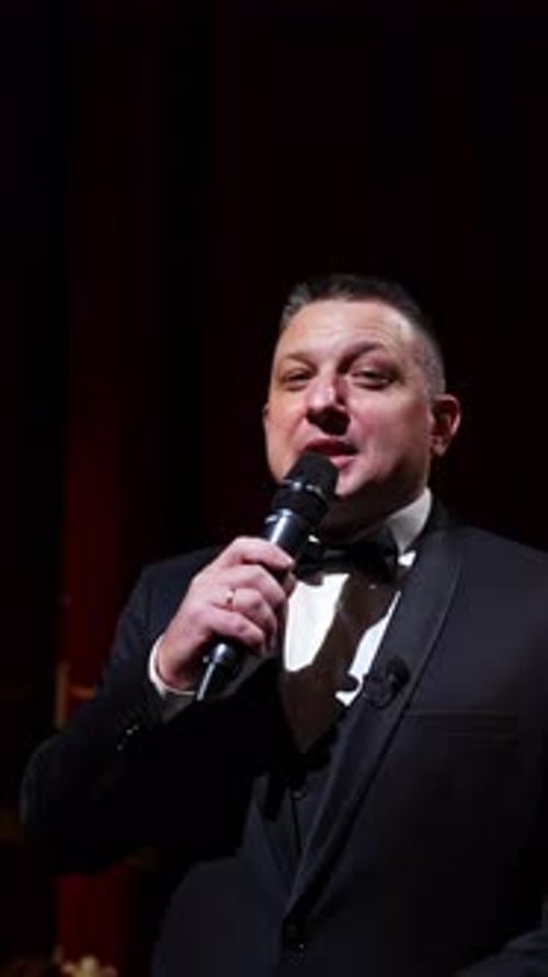 Presenter with microphone announces performance before auditorium from stage.
