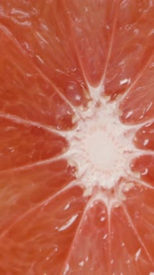 Vertical video. Macro zoom, a half of a grapefruit with red juicy flesh on a wooden table. Dolly.