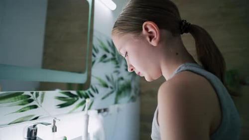 Jovencita mira al espejo en el baño y se cepilla los dientes