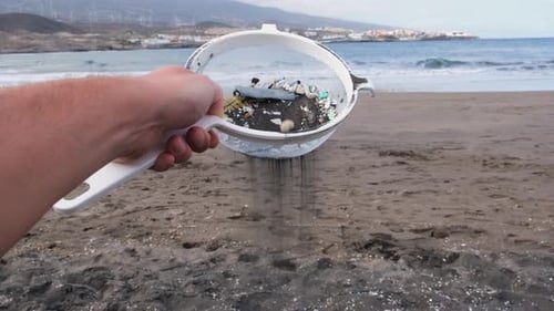 Young man cleans microplastics from sand on tropical beach pollution warning