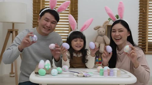Vater, Mutter und Tochter halten am Ostertag zu Hause ein buntes Ei zusammen