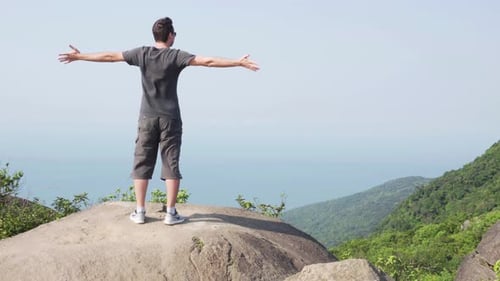 Man raising hands and enjoying wind on top of mountain