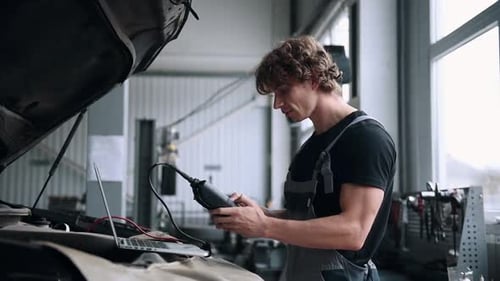 Computer diagnostics of cars, young mechanic specialist male uses laptop technology while repairing