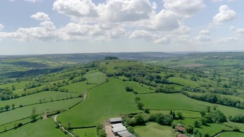 Sideways aerial of a solitary hill in a vast countryside landscape in late spring.