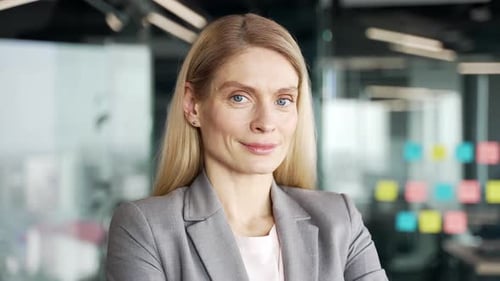 Portrait of a happy businesswoman in suit standing at workplace in business office. Smiling blonde