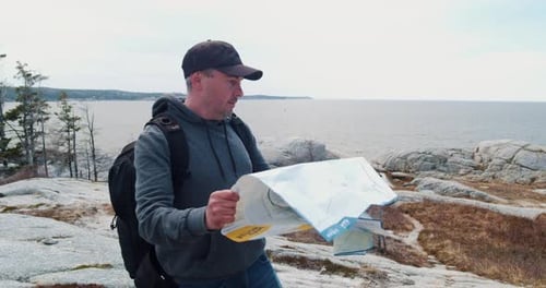Man Reads Map by Scenic Ocean Coastline