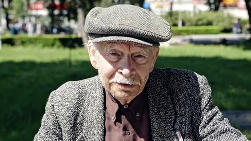 Portrait of Senior Elegant Man Wearing Jacket with Cap and Looking at Camera in Green Park in