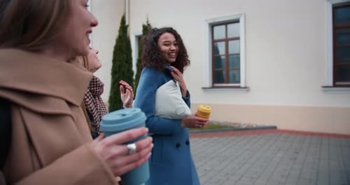 Side View Three Beautiful Happy Young Diverse Female Friends Walk Together with Eco Drink Cups Along