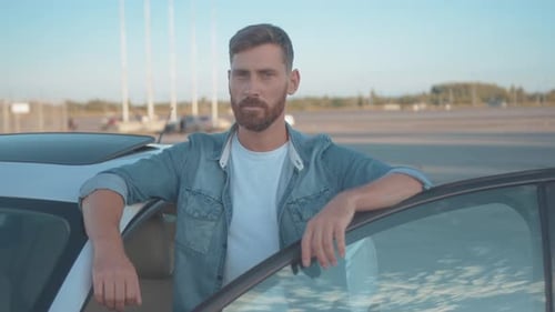 Bearded Young Adult Leans on Car and Smiles
