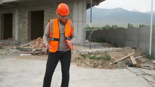 Trabalhador da construção civil dançando de bom humor ouve música em fones de ouvido, canteiro de obras