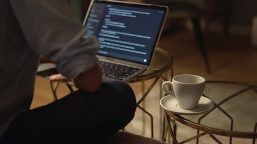 Eine Person konzentriert sich sehr darauf, auf ihrem Laptop zu programmieren, während sie die ganze Zeit eine warme Tasse Kaffee neben sich hat