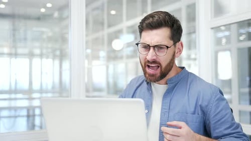 Angry businessman arguing talking on video call using laptop computer sitting at workplace in office