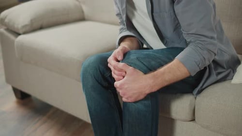 Adult Holding Knee While Sitting on Couch
