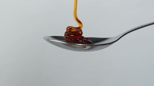 Sweet golden honey dripping, healthy liquid nectar flowing onto a metal spoon and dropping down.4k i