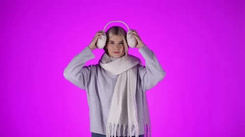 Woman Puts on Earmuffs in Front of Pink Backdrop
