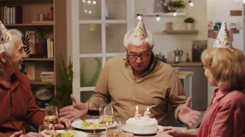 Elderly Birthday Man Blowing Out Candles on Cake when Celebrating 65 Years Old