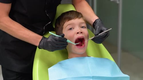 A Cute Boy with an Open Mouth is Looking to the Side While the Doctor is Treating Her Teeth