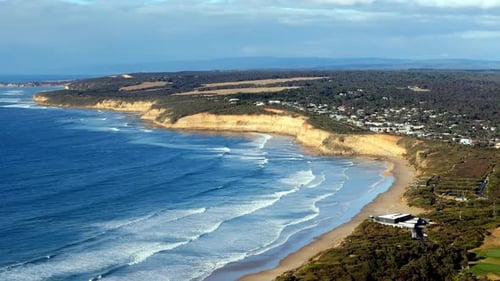 Coastal cliffs tower over a sweeping sandy beach, Waves gently breaking along the shoreline with a q