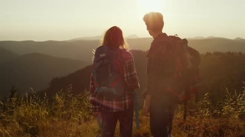Back View Male and Female Tourists Enjoying Sunset in Mountains. Happy Guy