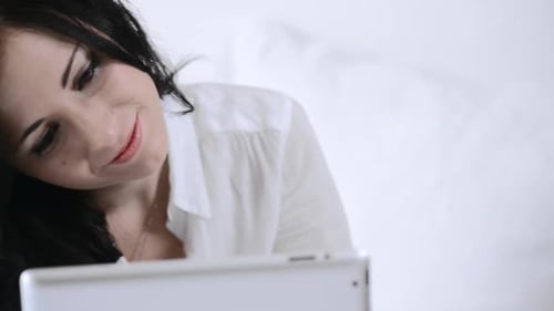 Smiling woman using tablet while relaxing in bed