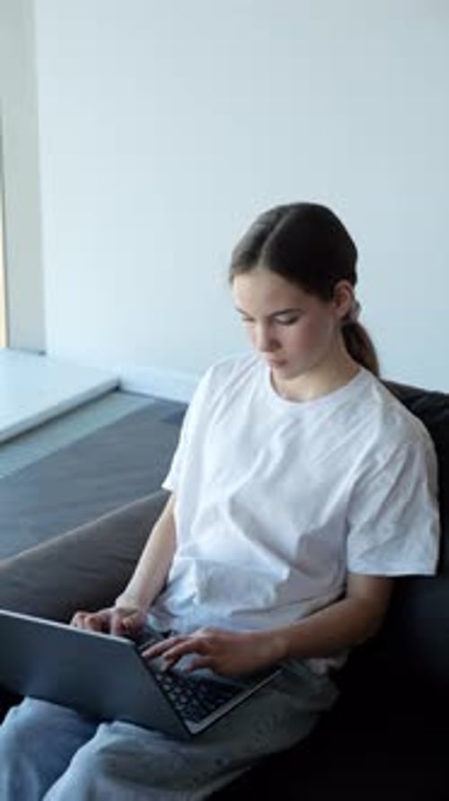 Mädchen sitzt mit Laptop auf dem Sofa und arbeitet an einem Schulprojekt