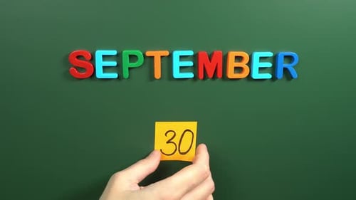 Hand sticking a sticker 30 September calendar day on school board. 30 date of September. Thirtieth