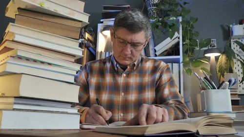 Mann studiert Buch am Schreibtisch mit großem Stapel Bücher in der Inneneinrichtung