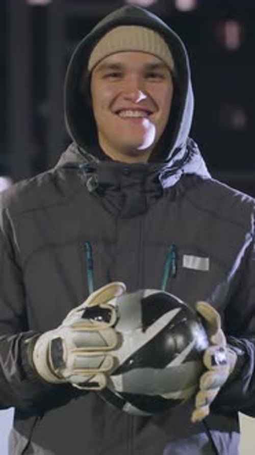 Smiling Athlete Holding Soccer Ball on Urban Sports Field at Night