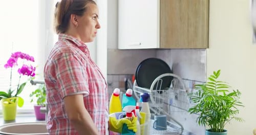 Eine müde Frau in gelben Gummihandschuhen wischt einen Tisch mit einem Lappen mit Reinigungsmitteln ab