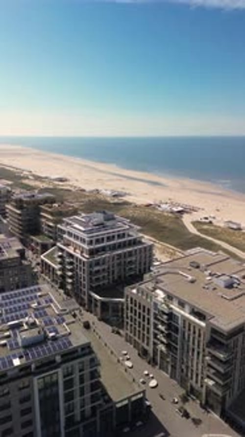 Aerial view of a modern beachside development with apartment buildings, sand dunes, and a wide sandy