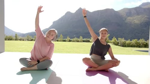 Practicing yoga, two women sitting on mats outdoors in serene mountain setting