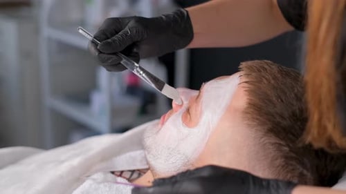 A Cosmetologist Performs a Facial Massage with a Clay Mask Applied to the Face A Man in a Spa