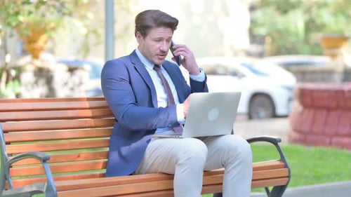 Man in Suit Works on Bench with Laptop