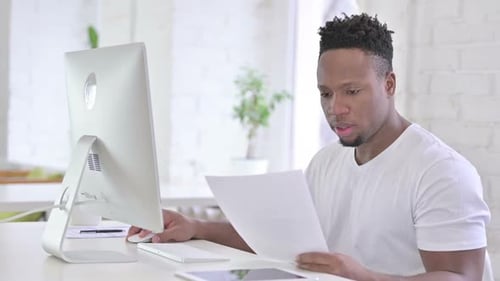 Casual African Man doing Paperwork with Desktop in Office