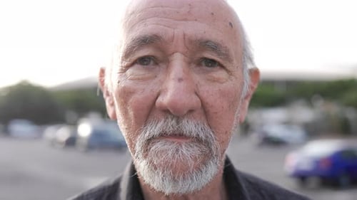 Asian senior man looking at camera with city street on background. Closeup face