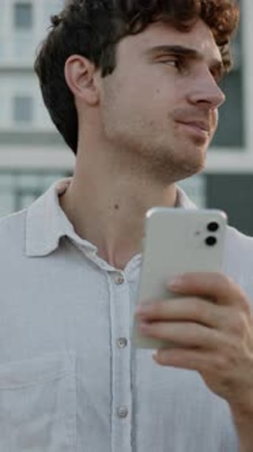 Pensive Man with Curly Hair Uses Smartphone Outdoors