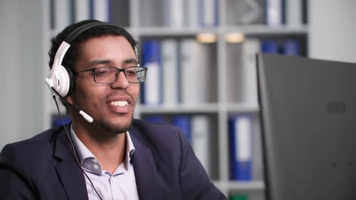 Charming African American Male Call Center Employee Puts on Headset to Talk with Client While