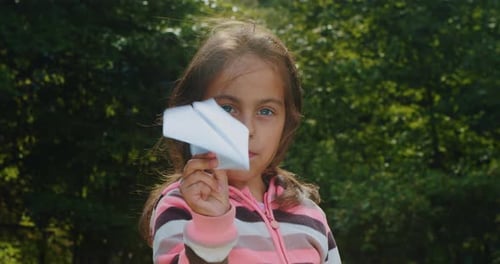 Cheerful Little Girl Plays with a Paper Airplane in the Forest in Summer