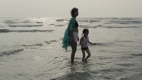 Young mother and child enjoying a serene walk in shallow sea waters, golden hour light
