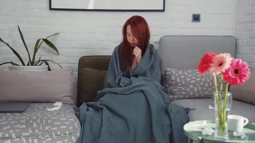 Femme asiatique froide et malsaine frissonnant enveloppée dans une couverture essayant de se réchauffer sur le canapé dans le salon