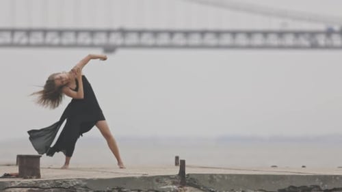 Woman Dances on Pier Near Bridge