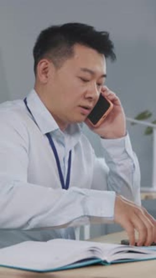 Man Talking on Two Phones and Writing Notes