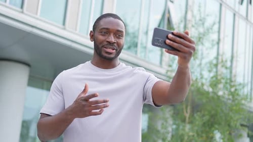 African American Man Holding Smartphone Having Video Chat on Urban Street in City Guy Blogger
