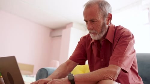Senior Man Typing On Laptop Inside Home