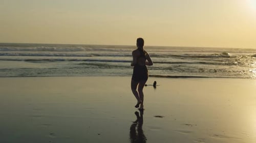 Young Sporty Caucasian Girl Running on the Beach During Sunset Slim Blonde Lady Runner Training