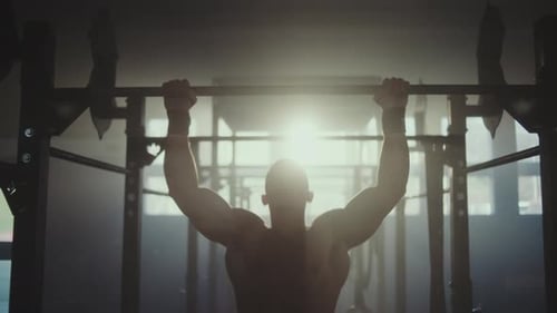 Man Doing Pull-Ups in Dark Gym