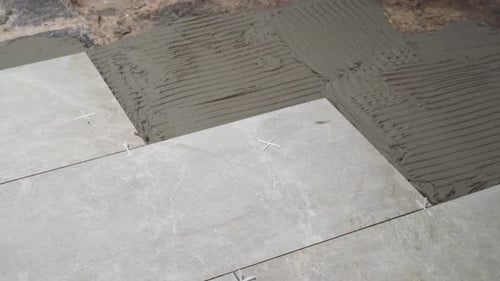 A close look at the construction tiler worker laying down the tile on cemented floor. Professional w