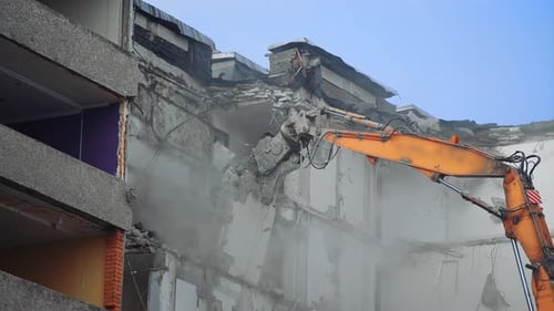 Excavator Demolishing Building in Dusty Urban Setting